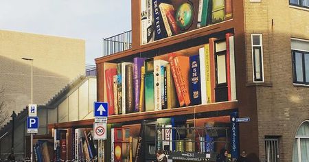 Un artiste peint sur un mur une bibliothèque géante avec les livres préférés des locataires de l'immeuble