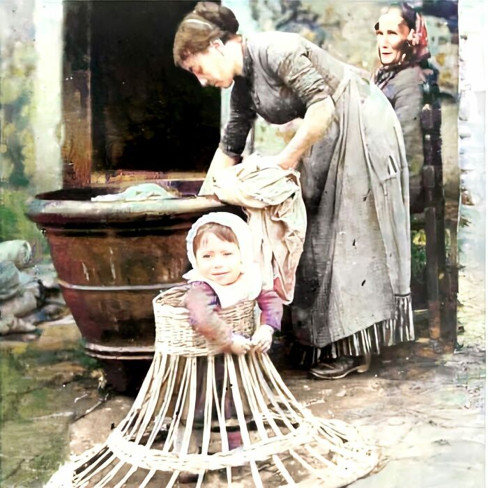 Un bébé apprend à marcher dans un cadre en osier pendant que maman fait la lessive. années 1910