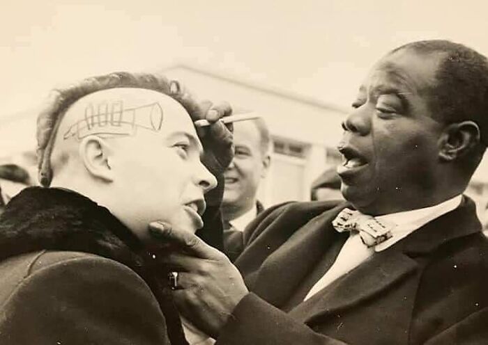 Le trompettiste américain , Louis Armstrong, qui dessin sur la tête d’un jeune homme à Nice en France, en 1961