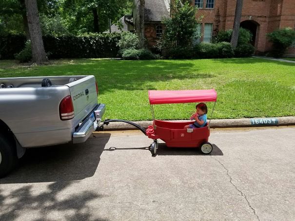 enfant tracté dans son chariot par son père en voiture